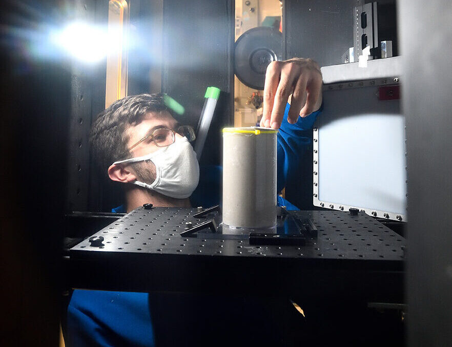 Researcher with mask leaning into a lit box to set up an experiment