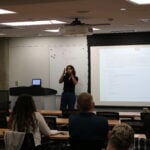 Individual giving lecture to class in front of projector screen