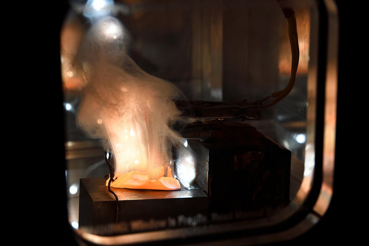 An orange material emits smoke as it smolders in a lab environment