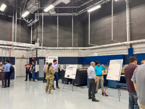 Students present research posters in a large indoor space.
