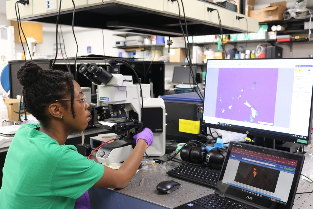 A researcher adjusts a microscope and looks at images of crystals on a computer.