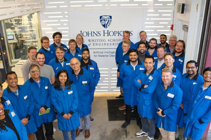 a large group of people wearing lab coats stands in front of the Artificial Intelligence for Materials Design Laboratory