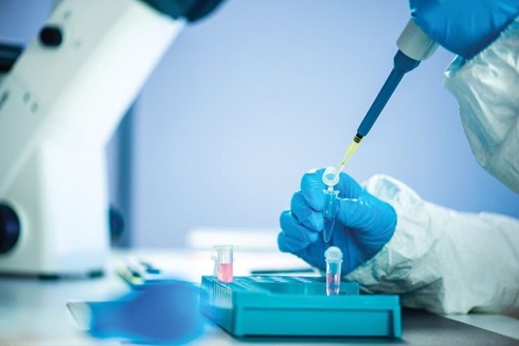 Researcher wearing gloves and using a pipette to transfer liquid into a microcentrifuge tube.